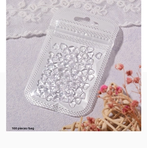 Detail view of 100pcs transparent resin heart nail charms in a clear poly bag