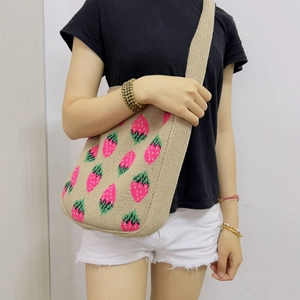 Close-up of beige knitted tote bag featuring pink strawberry patterns and wide shoulder strap