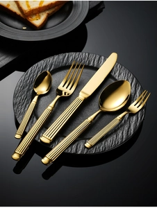 Macro shot of 5-piece gold stainless steel cutlery set with elegant fluted handles on black plate