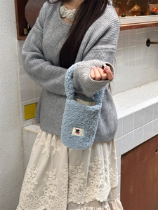 Close-up of a light blue plush tote bag with a cartoon patch on a model outfit