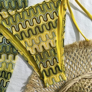 Détail du bas de bikini au crochet ondulé jaune et vert sur fond blanc texturé
