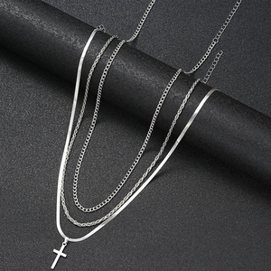 Detail of silver layered necklace with snake chain and minimalist cross pendant
