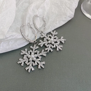 Close-up of snowflake hoop earrings with pearl center and sparkling rhinestones