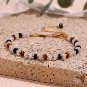 Macro detail of tiger eye and white jade beads on a gold-plated stainless steel bracelet