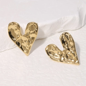 Close-up of golden heart earrings with hammered texture on white stone base