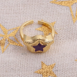 Macro detail of gold star ring with purple enamel inlay on a sparkling fabric background