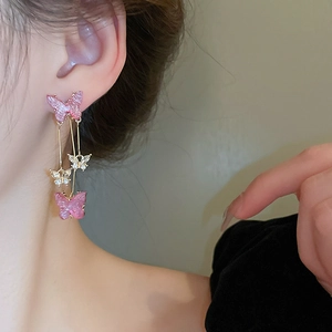 Détail des boucles d'oreilles papillon avec ailes scintillantes et longues chaînes dorées