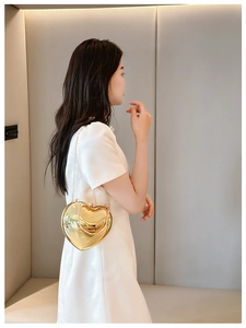 Close-up of heart-shaped gold acrylic bag with metallic chain on shoulder