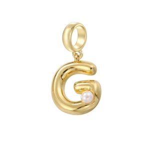 Détail d'un pendentif lettre G doré vintage avec une perle blanche sur fond blanc pur