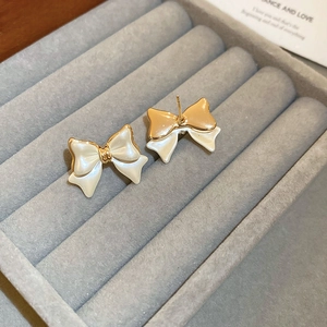 Detail of gold-plated bow earrings with white resin inlay on grey velvet jewelry display