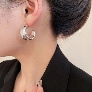 Macro shot of silver C-shaped wide hoop earrings with smooth liquid metal finish
