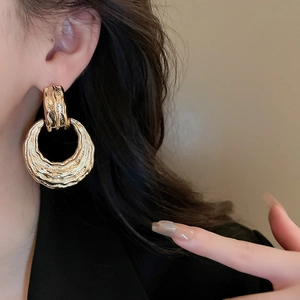 Detail of gold geometric earrings with textured metallic finish on model's ear