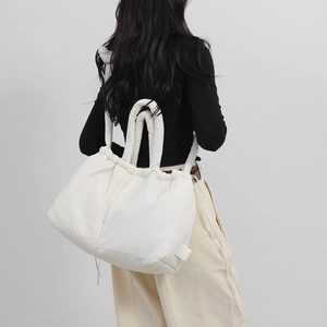 Minimalist beige quilted nylon drawstring tote bag worn by a model in a casual street style