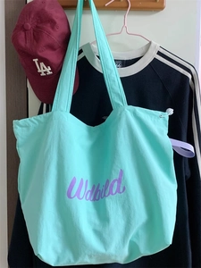 Detail of drawstring mint canvas tote bag with purple lettering hanging on a wooden hook