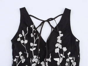 Détail du dos d'une robe noire avec broderies florales blanches et bretelles nouées