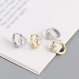Macro detail of cat paw huggie earrings with heart zircon in gold and silver plating