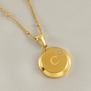 Detailed close-up of 18K gold letter C pendant with sparkling crystal on a bead chain