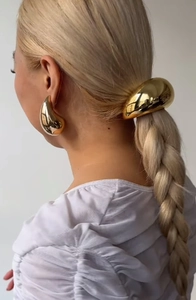 Detailed view of polished golden metal hair band and teardrop earrings on model