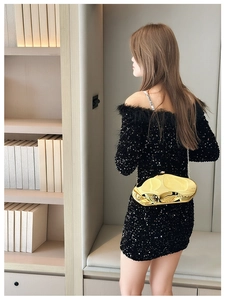 Detailed view of an irregular gold metallic clutch bag against a black sequin evening dress