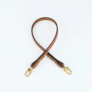 Close-up of tan lychee leather shoulder strap with white stitching and gold buckles