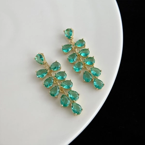 Détail macro de boucles d'oreilles fleur dorées avec pierres de zircon vert goutte