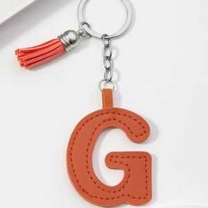 Detail view of an orange PU leather letter G keychain with silver ring and tassel accessory