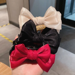 Close-up of three satin bow hair claws in red, black, and cream with smooth silk texture