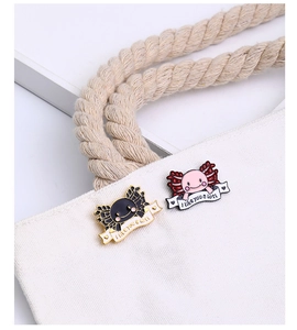 Detail view of cute pink and black axolotl enamel pins on a white canvas bag