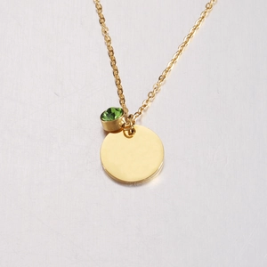 Close-up of golden mirror-finish round pendant with an inlaid green gemstone charm