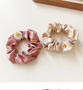 Detailed view of two silk satin scrunchies with white daisy patterns in rose and gold