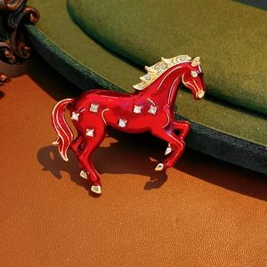 Detail of red enamel horse brooch with sparkling crystals on green velvet surface