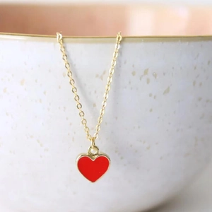 Minimalist gold chain necklace featuring a glossy red enamel heart pendant on a white bowl