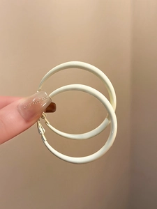 Detail view of large cream enamel hoop earrings with smooth matte finish held in hand
