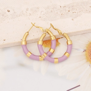Detail of gold hoop earrings with purple enamel sections on a stone background