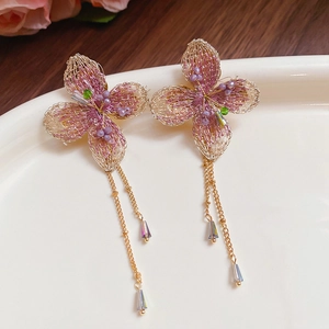 Dettaglio di orecchini a fiore intrecciato con petali rosa e nappe in cristallo