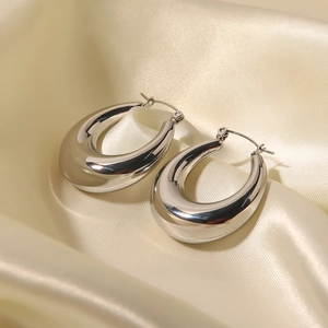 Detailed view of thick U-shaped silver hoop earrings on elegant silk fabric background