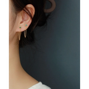 Close-up of golden tassel earrings with green and teal gems on a female model