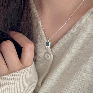 Detail view of a 925 silver necklace with an oval green gemstone on a knit cardigan