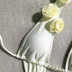 Detailed macro view of 3D rose floral accents and faux pearl beads on white swimwear