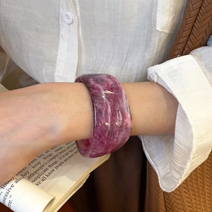 Close-up of a wide resin bangle with purple marble texture worn on a wrist over books