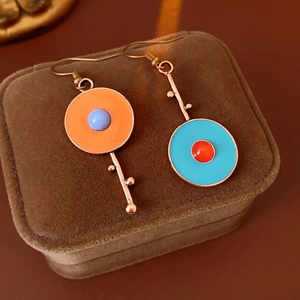 Macro shot of asymmetric vintage enamel earrings with orange, blue, and red floral details