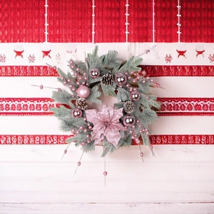 Detail of pink Christmas wreath with frosted pine needles, shiny ornaments and large flower