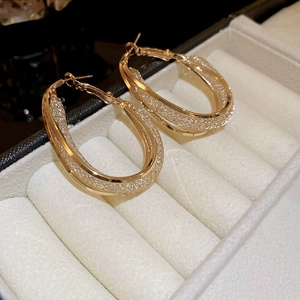 Macro detail of gold oval intertwining earrings with shimmering textured inner finish