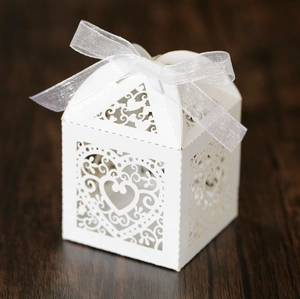 Detail of white laser-cut heart candy box with silver ribbon on wooden background