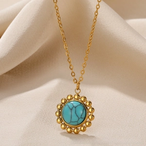 Close-up of 18k gold pendant with turquoise stone inlay on a soft beige fabric
