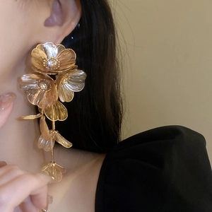 Detail of long floral drop earrings with layered petals and gold trim on model