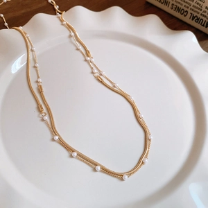 Detail of a layered gold snake chain necklace with white pearls on a ceramic tray