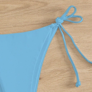Light blue string bikini bottom with adjustable side ties on a light wood background