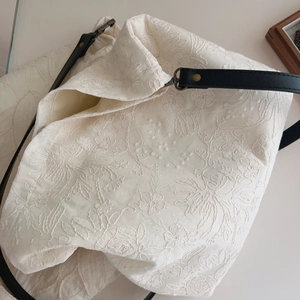 Detailed close-up of beige cotton tote with floral embroidery and black leather strap