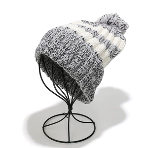 Detail of grey and white chunky knit beanie with a fluffy pompom on a display stand